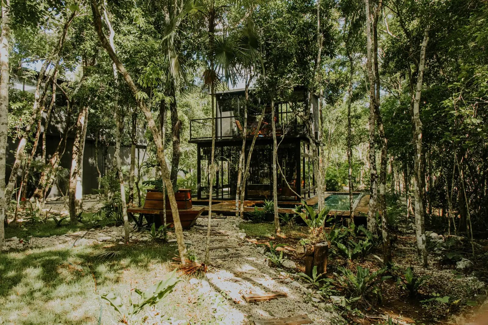Casa contemporánea de vidrio y estructura oscura con alberca, entre la selva de Tulum.